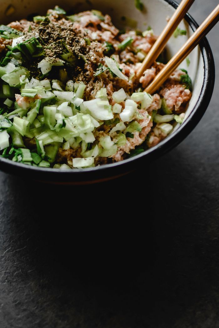 Close-up of a bowl filled with uncooked minced pork, chopped vegetables, and spices, ready for cooking.